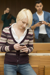 Zwei Studentinnen und ein Student telefonieren und schreiben SMS