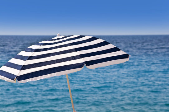Photo d'un parasol classique &agrave; rayures blanc et bleu sur fond de mer sur la plage de Nice, France. Vacances &agrave; la plage.