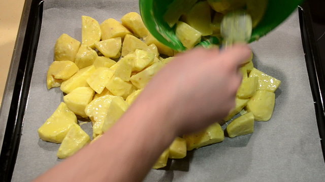 hands put spiced sliced potatoes in baking pan. food prepare
