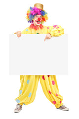 Full length portrait of a happy male clown pointing on a panel