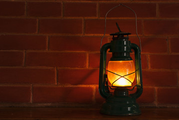 An oil lamp lantern lighting in front of a brickwall background.