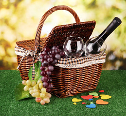 Picnic basket and bottle of wine on grass on bright background