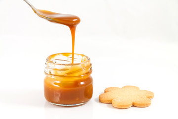 Pouring caramel in a small jar with a spoon with a cookie next t