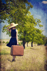 Redhead girl with suitcase at tree's alley.