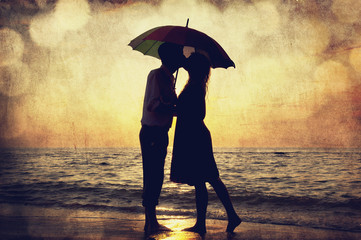 Couple kissing under umbrella at the beach in sunset. Photo in o