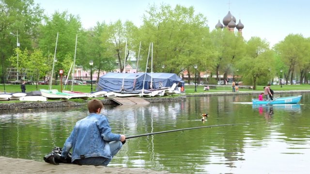 Fisherman on pond in city park, family sail on boat