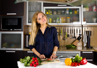 Young pretty blond woman cooking fish in kitchen