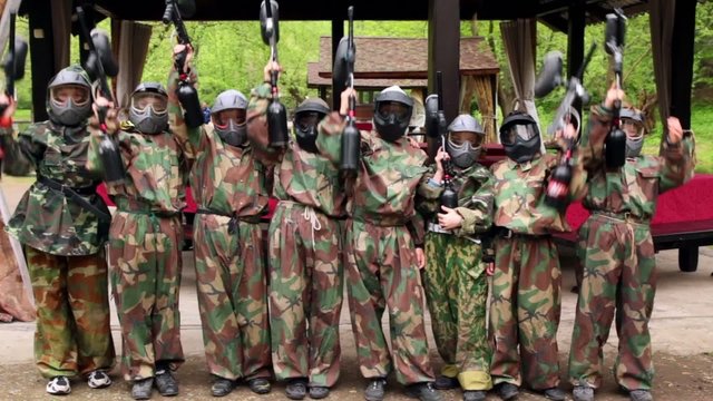 Eight teenagers paintball team stand and aim weapon