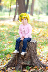 beautiful little girl in a wreath of maple leaves sitting on stu