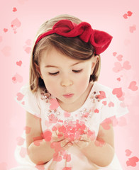 Little girl blowing heart confetti on pink background
