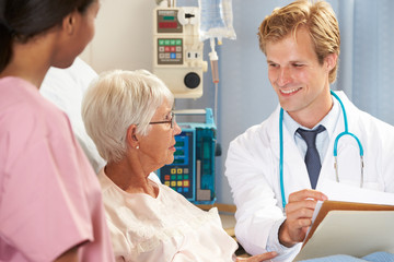 Doctor With Nurse Talking To Senior Female Patient In Bed