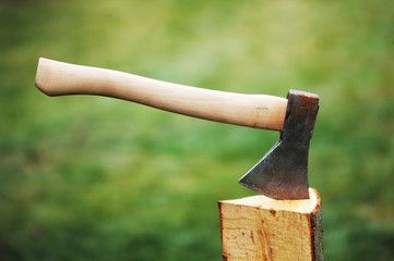 Axe in a log on the background of green grass