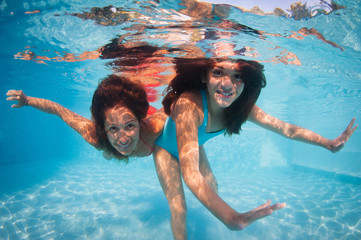 Mother and daughter having fun underwater in swimming pool.