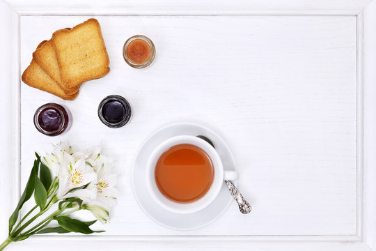 breakfast table with tea, cup of tea, flower, jam and bread