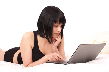 Cute young female lying with laptop in the bed