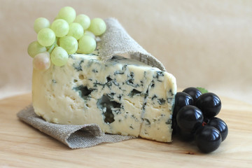 Slice of blue cheese with grapes on wooden background, close-up