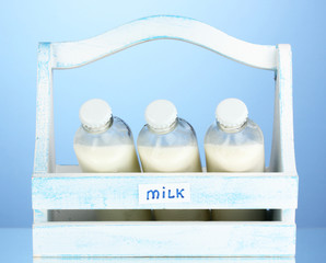 Fototapeta na wymiar Mleko w butelkach w drewniane pudełko na niebieskim tle