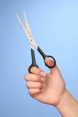 Female hand with scissors on color background