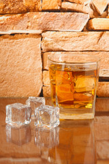 Glass of whiskey and ice on brick wall background