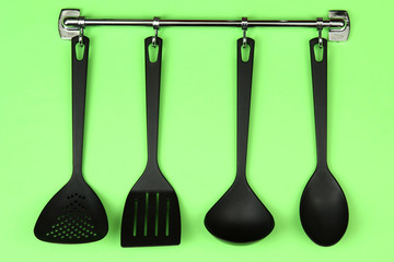 Black kitchen utensils on silver hooks, on green background