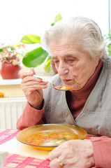 Happy old gray-haired woman eating soup