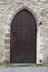 Fototapeta na wymiar Medieval brown wooden door with black handle and stone wall