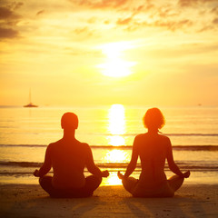 Young couple in a lotus position meditating on the beach