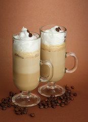 Fragrant coffee latte in glasses cups, on brown background