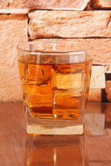 Glass of whiskey and ice on brick wall background