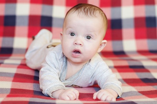 The surprised baby lying on a red checkered plaid