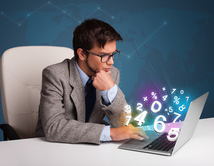 Handsome man sitting at desk and typing on laptop with 3d number