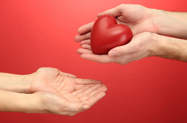 Red heart in woman and man hands, on red background