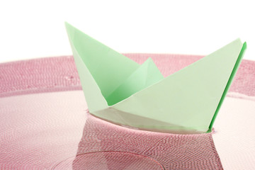 Color paper ship in water on pink plate, close-up