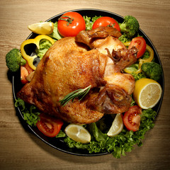 Whole roasted chicken with vegetables on plate, on wooden table