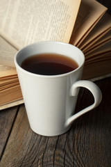 Cup of tea with old opened book on wooden table.