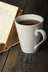 Cup of tea with old opened book on wooden surface.