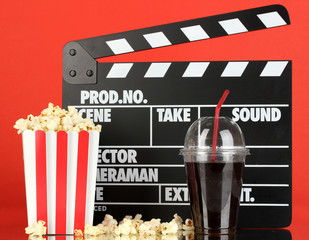 Movie clapperboard, cola and popcorn on red background