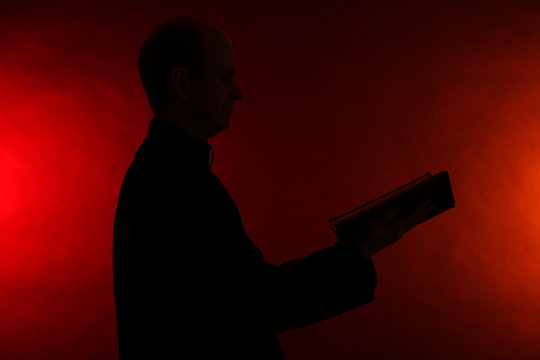 Young Pastor With Bible, On Dark Red Background