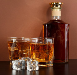 Bottle and Glasses of whiskey and ice on brown background