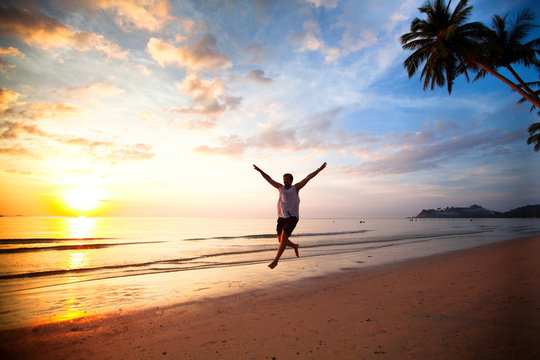 Young fun man running on sea beach at sunset