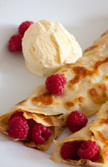 Crepes with raspberries and vanilla ice cream on a white plate