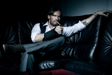 Sexy brunette man on the black couch smoking a cigarette