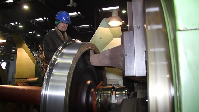 Worker processing steel on lathe in a factory