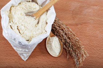 Corn flour in a bag with wooden spoon and ear on wooden table.