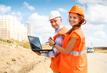 female and male construction workers looking at laptop against