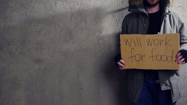 homeless man standing at the wall with a cardboard