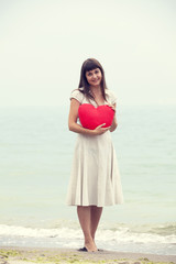 Fototapeta na wymiar Brunette girl holding toy heart at the beach.