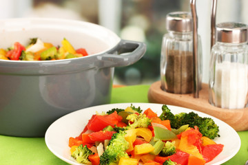 Vegetable stew in gray pot on wooden table on bright background