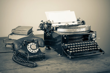 Vintage phone, old typewriter, books on table desaturated photo