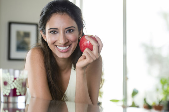 Indian woman holding apple in kitchen